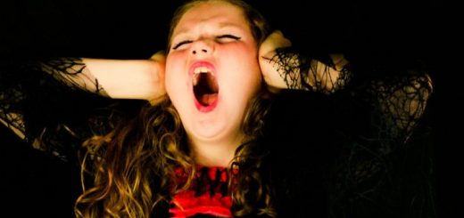 A lady in black and red shouting and closing her ears.